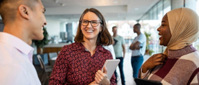 Three colleagues engaged in conversation inside a modern office building.