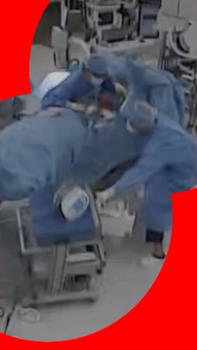 View of an operating room with a patient lying down surrounded by staff in blue scrubs