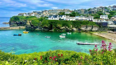 Cornwall coastal scene with crystal-clear water, sandy beach, fishing village and blue sky 


