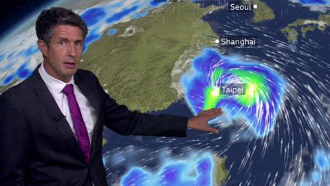 A weather presenter stands in front of a screen showing heavy rains over Taiwan