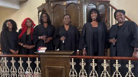 A choir stands together at the pulpit, ready to deliver a performance