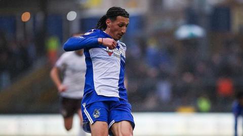 Yusuf Akhamrich in royal blue and white Bristol Roves kit looks down to control the ball