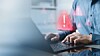 A person typing on a laptop with a red warning triangle icon displayed on the screen.