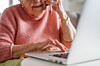 Older woman typing on a laptop while seated indoors at a table.