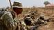 A US soldier leans standing against a rod while two Nigerian soldiers conduct a military exercise while laying on the ground A US soldier leans standing against a rod while two Nigerian soldiers conduct a military exercise while laying on the ground
